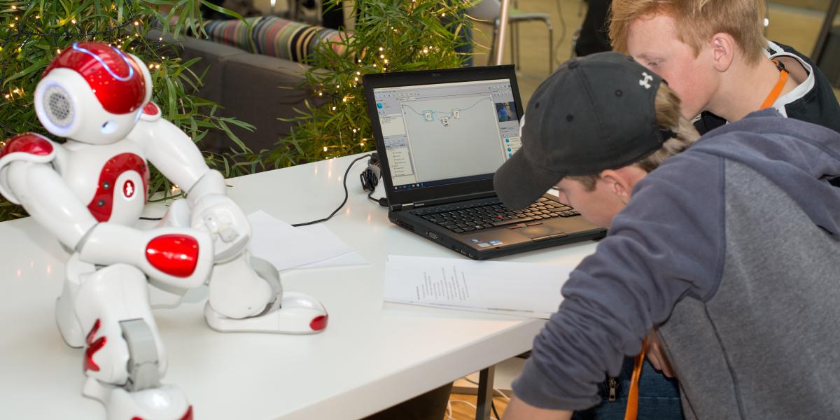 Billedet viser to unge, der via en PC programmerer en robot.
